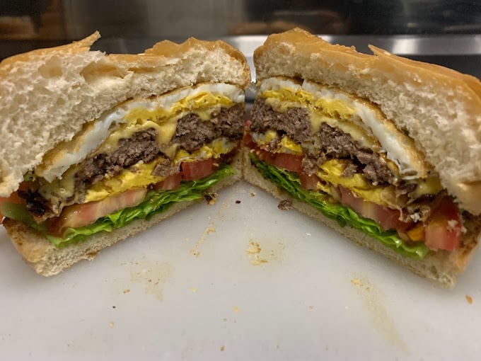Lanche cortado no meio recheado com pão, ovo, carne, queijo, alface, tomate e molho.